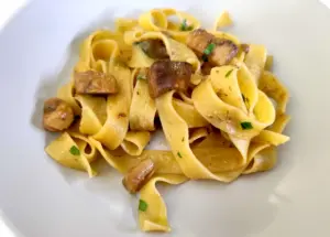 Pappardelle ai funghi porcini cremose con porcini dorati e prezzemolo fresco servite in un piatto chiaro, fotografia food professionale luminosa.